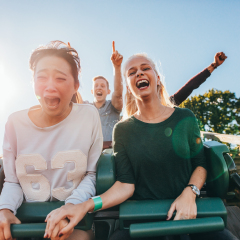 Enthusiastic young friends riding roller coaster ride at amusement park. Young people having fun at amusement park.