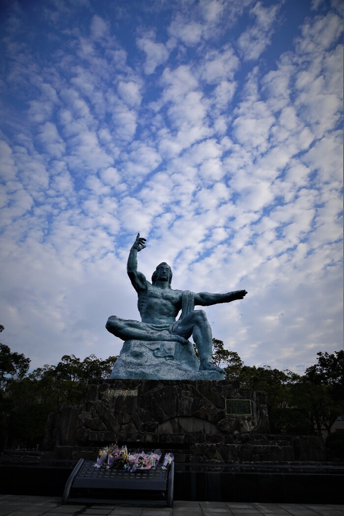 雕像双目紧闭,似为罹难者祈祷;右手指向天空,示意从天而降的核威胁