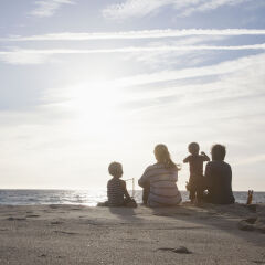 Back view of familiy with two kids sitting on the beach at twilight
