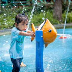 Child little girl having fun to play with water in park fountain in summer time