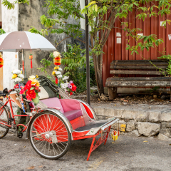 An old rickety trishaw cab parked on the sidewalk of a dilapidated building in Penang, Malaysia.