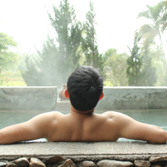 Asian man relaxing in outdoor japanese hot bath.