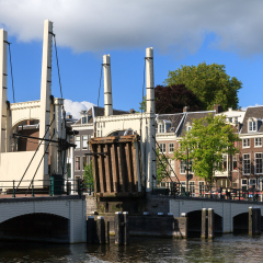 Beautiful unique view of the skinny bridge (magere brug) while open at the river Amstel in Amsterdam, the Netherlands, on a sunny summer day with blue sky and some clouds 
