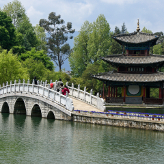 LIJIANG, YUNNAN, CHINA, APRIL 25, 2009. People walk across an arched stone bridge at Black Dragon Pool Park, next to a tile-roofed, three-tier pagoda, on a sunny day in springtime.