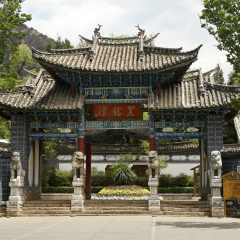 LIJIANG, YUNNAN, CHINA, APRIL 25, 2009. An ornate painted gate with peaked tile roof, guarded by stone lions, marks the entrance to Black Dragon Pool Park on a sunny day in springtime.