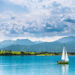 Sailboat on lake Forggensee, Bavaria, Germany, under glowing, cloudy sky.