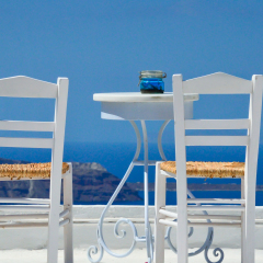 Two white chairs and a blurred panoramic view of the volcano of Santorini, Greece.