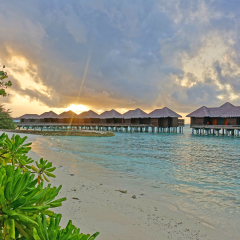 NORTH MALE, MALDIVES -6 JUL 2018- Sunset view of luxury over the water bungalows with thatched roofs at the Sheraton Maldives Full Moon Resort & Spa hotel on Furanafushi Island, North Malé Atol.