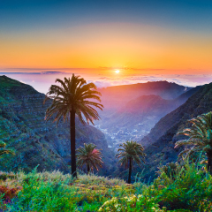 Beautiful view of amazing tropical scenery with exotic palm trees and mountain valleys above wide open sea in golden evening light at sunset with blue sky and clouds in summer, Canary Islands, Spain