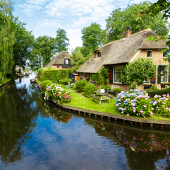 Landscape view of famous Giethoorn village with canals and rustic thatched roof houses in farm area.