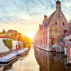 Bruges, Belgium. Medieval ancient houses made of old bricks at water channel with boats in old town. Summer sunset with sunshine. Picturesque landscape.
