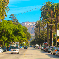 Hollywood sign district in Los Angeles, USA. Beautiful Hollywood highway road with cars, palms and a sign on the hills. Clear blue sky.