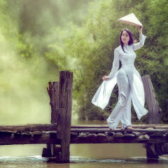 Vietnames cute girl in national dress standing on a wood bridge.
