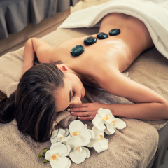 High angle view of young woman lying down on massage bed with traditional hot stones along the spine at spa and wellness center