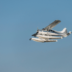 Seaplane, flying boat on clear blue sun sky background, side