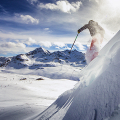 Free ride skier, skiing down steep slope, good background with blue skies and mountains
