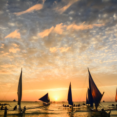 Several tourists are enjoying the spectacular sunset on the island of Boracay seated on typical Philippines boats.