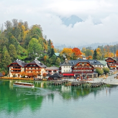 A sightseeing boat cruising on Konigssee ( King's Lake ) surrounded by colorful autumn trees and boathouses on a foggy misty morning~ Beautiful scenery of Bavarian countryside in Berchtesgaden Germany