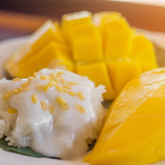 The close up of sticky rice and heap yellow mango by restaurant style setting in the dish with the green banana leaf under in the natural light. 