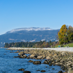 VANCOUVER, BC - NOVEMBER 2017: People walking and enjoying the view on the seawall at English bay with Stanley park and mountains in the background.