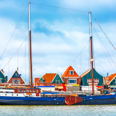 Fishing village Volendam panoramic view Holland Netherlands with antique ship small wooden houses on coast lake Markermeer sunny day blue sky clouds.