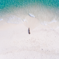 Young woman in a bikini lying on the back on the white sand near the waves of blue sea. Top view. Kai island, Andaman Sea, Phuket, Thailand. Aerial Shooting.