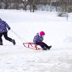 Winter activities outdoors. Elder girl running and pulling her young sister on a sled on the ice in snowy winter park
