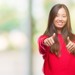 Young asian woman wearing winter sweater over isolated background approving doing positive gesture with hand, thumbs up smiling and happy for success. Looking at the camera, winner gesture.