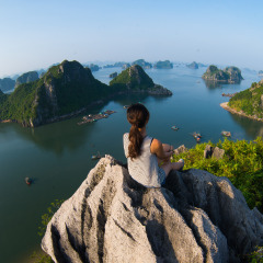 A young traveler girl sit on the top of mountain in Halong bay and enjoy the beauty of seascape. Young girl love wild life, travel, freedom.