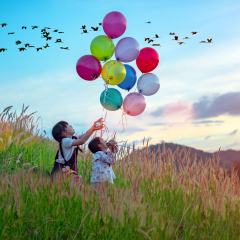 group of Happy little girls holding colorful balloons. Child playing on a green meadow. Smiling kid, beautibull sky sunset and flock of bird in backbround