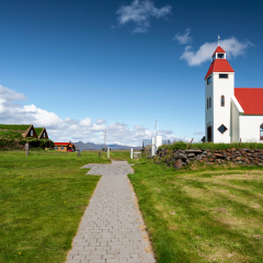 Walk pass to the church of Modrudalur at right and traditional turf houses at left in Eastern Island. Fljotsdalsherad municipality of Austurland.