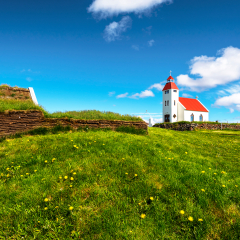 View at the church of Modrudalur settlement in Eastern Island, green grassland and the wall of traditional icelandic turf construction are at foreground. Fljotsdalsherad municipality of Austurland.