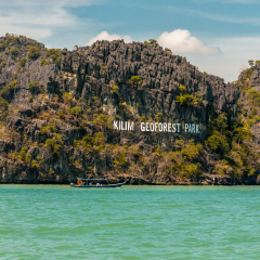 Beautiful scenery of a motorboat with tourists passing by the big limestone formation with the "Kilim Geoforest Park" sign. Taken in Febuary 2016, Langkawi, Malaysia.