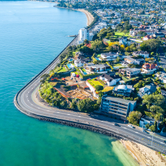 Aerial view on a road running along sea shore with residential suburbs on the background. Auckland, New Zealand.