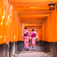 women geishas among red wooden Tori Gate at Fushimi Inari Shrine in Kyoto, Japan