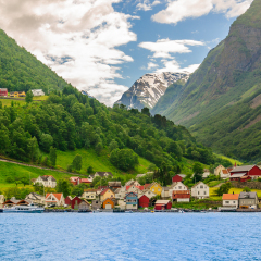 A lots of little colorful traditional Norwegian houses near the sea with green forest on mountains on background and blue sky with dark clouds, Sognefjord, Norway