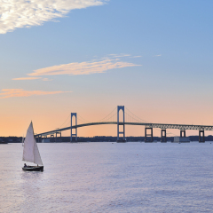 Sunset Newport Bridge sailboats Newport Rhode Island USA. Person in sailboat is in silhouette also changed face and body shape, clothing, hair (person was bald) so they are totally unrecognizable
