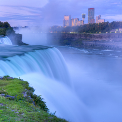 Flowing Niagara Falls from the American side with the skyline of the city of Niagara Falls in the background at dawn. The Niagara Falls is one of the largest and most famous waterfall in the world.